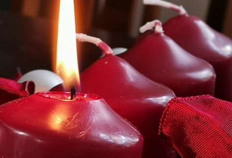 Vier rote Adventskerzen in Reihe und die erste Kerze brennt.