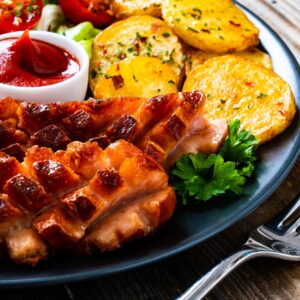 Krustenbraten mit Rautenschwarte auf Teller mit Kartoffeln und Dip