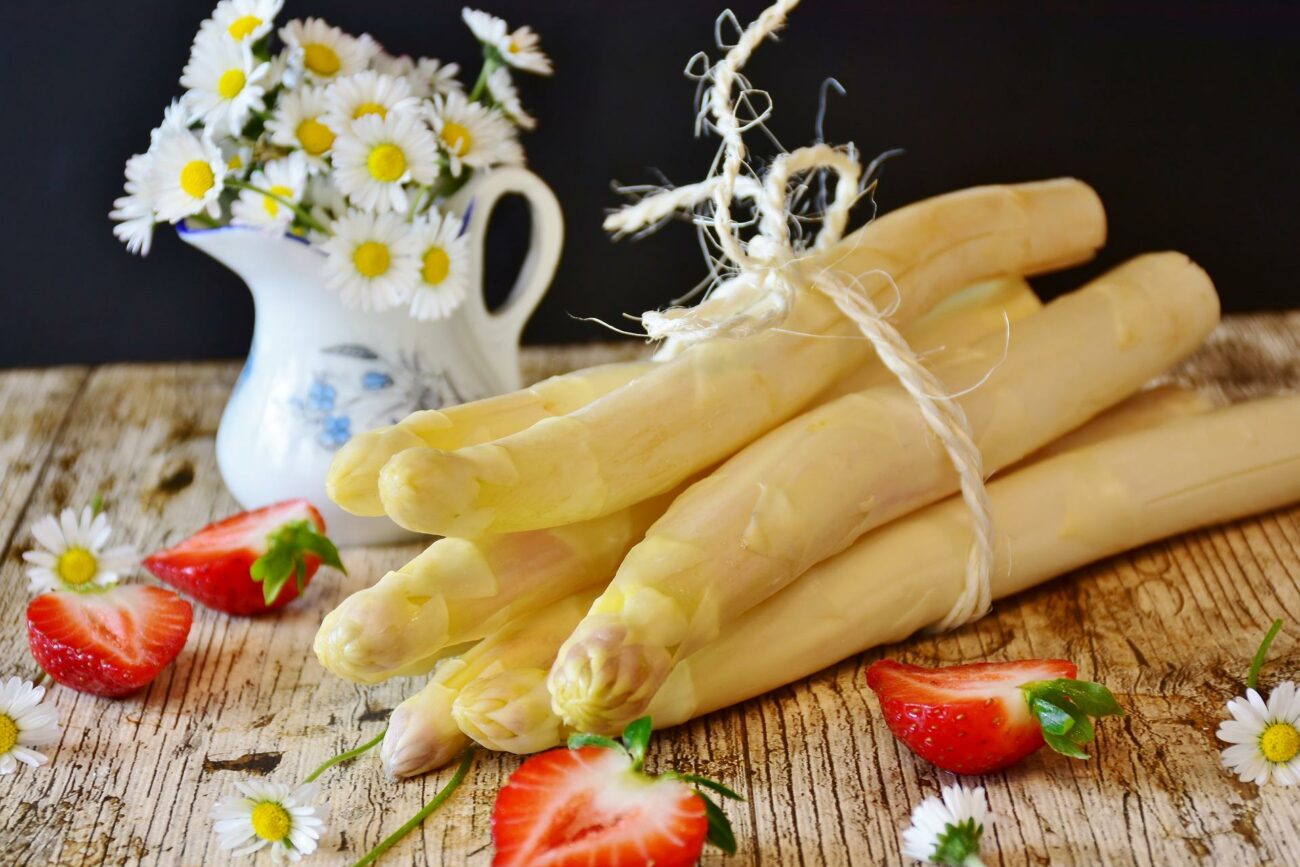 Weiße Spargelstangen gebündelt auf Brett auf, mit kleinem Milchkännchen mit Gänseblumen