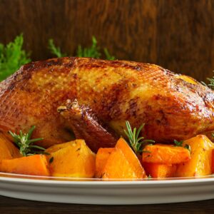 Seitenansicht: Ganze gebratene Gans auf einer Platte mit Gemüse rundum