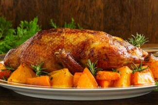 Seitenansicht: Ganze gebratene Gans auf einer Platte mit Gemüse rundum