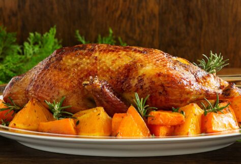 Seitenansicht: Ganze gebratene Gans auf einer Platte mit Gemüse rundum