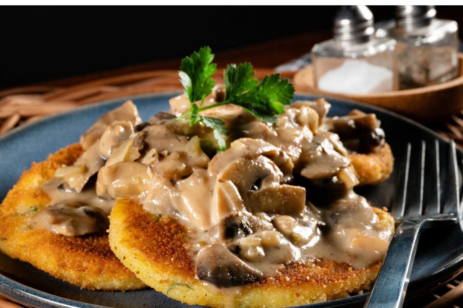 Zwei panierte Schnitzel mit Pilzrahmsoße auf Teller