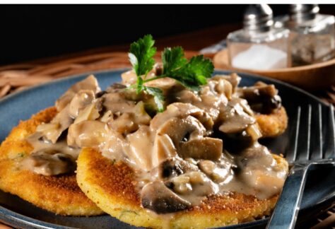 Zwei panierte Schnitzel mit Pilzrahmsoße auf Teller