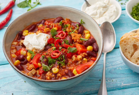 Hellblaue Bowlschale mit Chili sin Carne. Rechts davon Eßlöffel angelegt